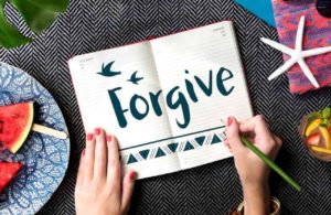 Woman writing "Forgive" in her diary - The Who, What, and How of Forgiveness