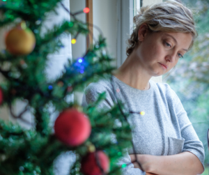 Woman looking at Christmas tree with a sad expression on her face.