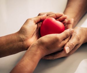 A hand giving a heart plushie to other hands